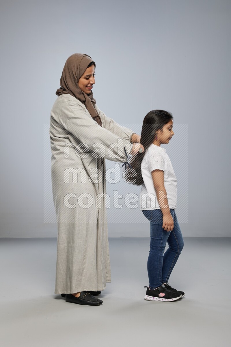 Mom standing styling hair for her daughter on gray background