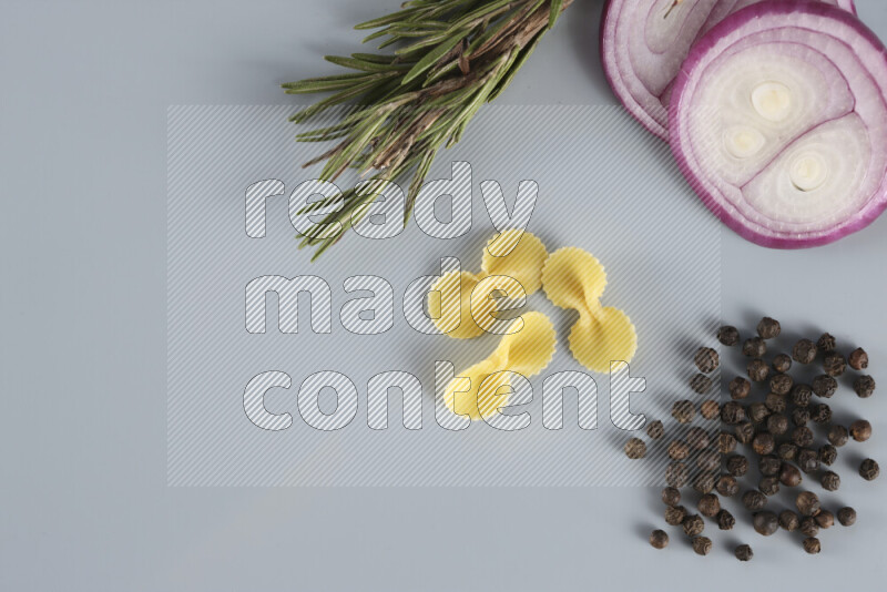 Raw pasta with different ingredients such as cherry tomatoes, garlic, onions, red chilis, black pepper, white pepper, bay laurel leaves, rosemary, cardamom and mushrooms on light blue background