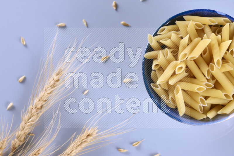 Raw pasta with wheat stalks on light blue background