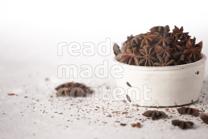 Star Anise in a white bowl and more of it sprinkled on white background