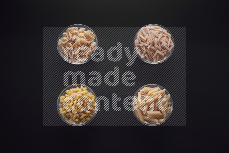 Different pasta types in glass bowls on black background