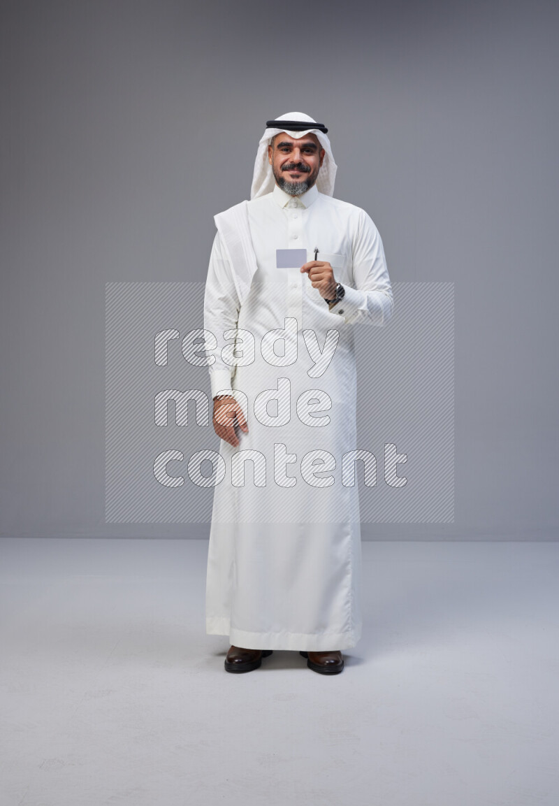 Saudi man Wearing Thob and white Shomag standing holding ATM card on Gray background