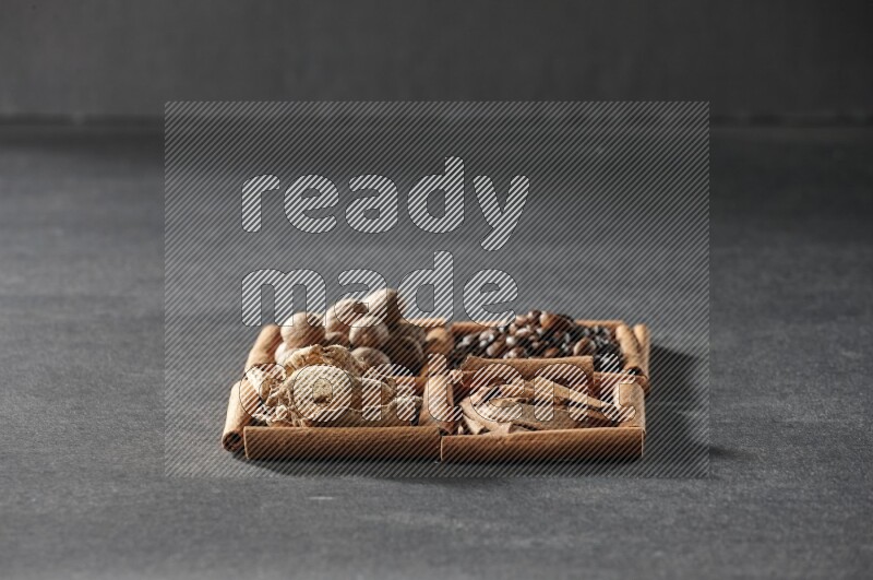 4 مربعات من عيدان القرفة ممتلئة بحبوب القهوة وقطع القرفة والزجبيل المجفف وجوزة الطيب على أرضية سوداء