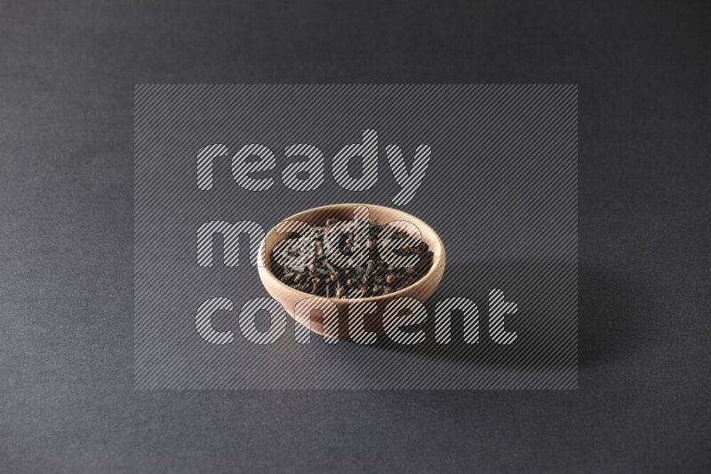 A wooden bowl full of cloves on a black flooring