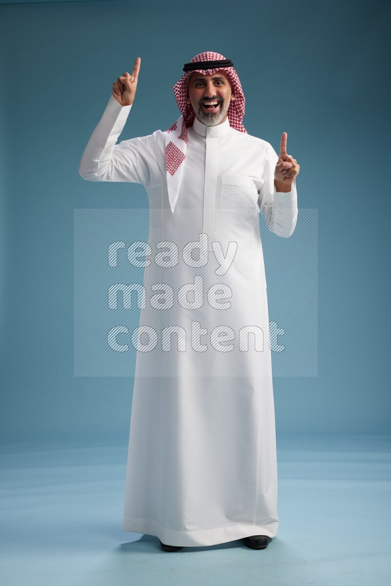 Saudi man wearing thob and shomagh posing to the camera on blue background