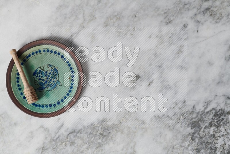 Decorative pottery plate with wooden honey dipper in it on grey marble background