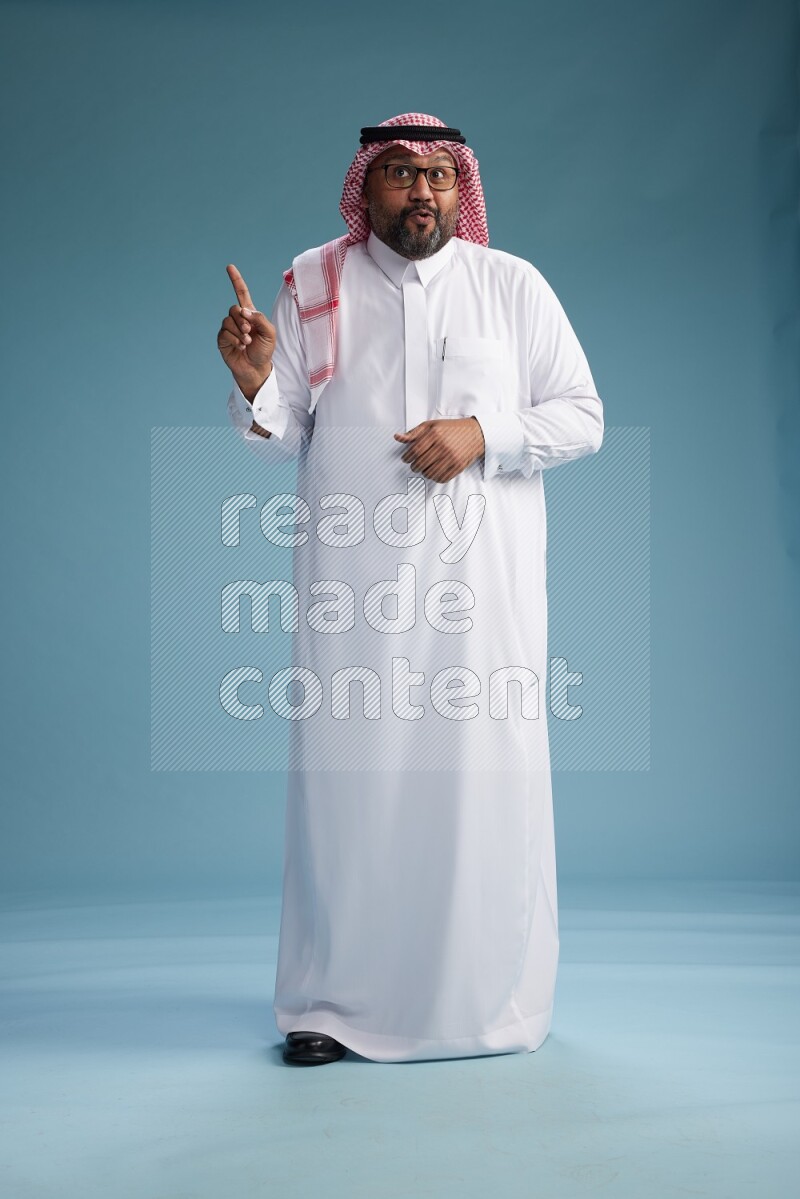 Saudi Man with shimag Standing Interacting with the camera on blue background