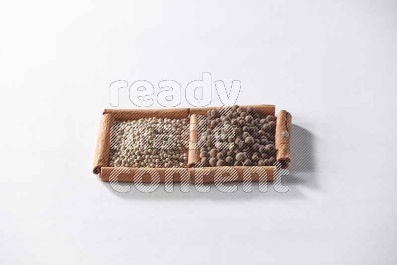 مربعان من أعواد القرفة ممتلئان بحبوب الفلفل الأبيض وحبوب الفلفل الحلو علي خلفية بيضاء