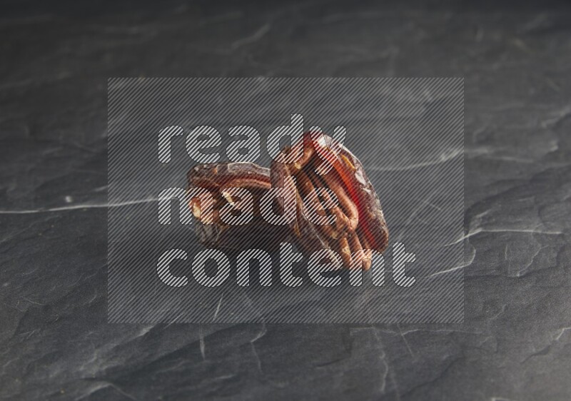 two pecan stuffed madjoul dates on a black textured background