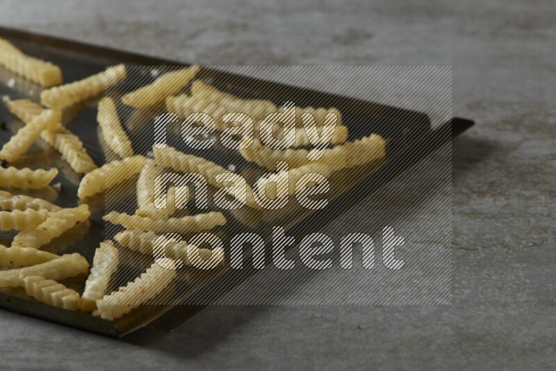 crinkle fries in a black stainless steel rectangle tray on grey textured counter top