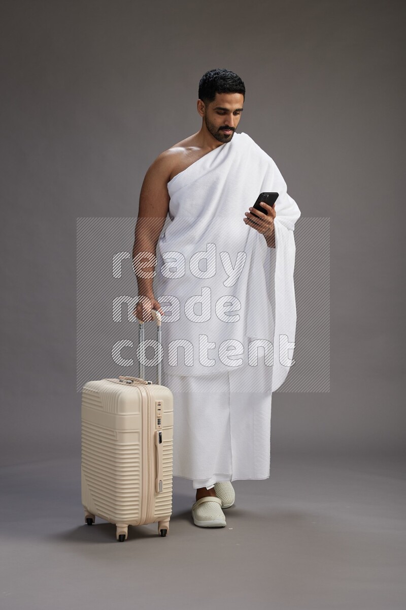 A man wearing Ehram Standing holding traveling bag on gray background