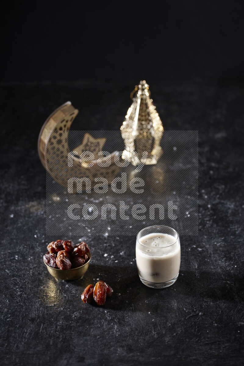Dates in a metal bowl with dates smoothie beside golden lanterns in a dark setup