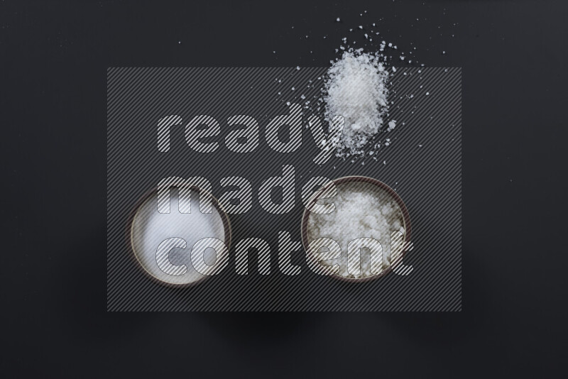 Pottery bowl full of fine table salt and coarse sea salt on black background