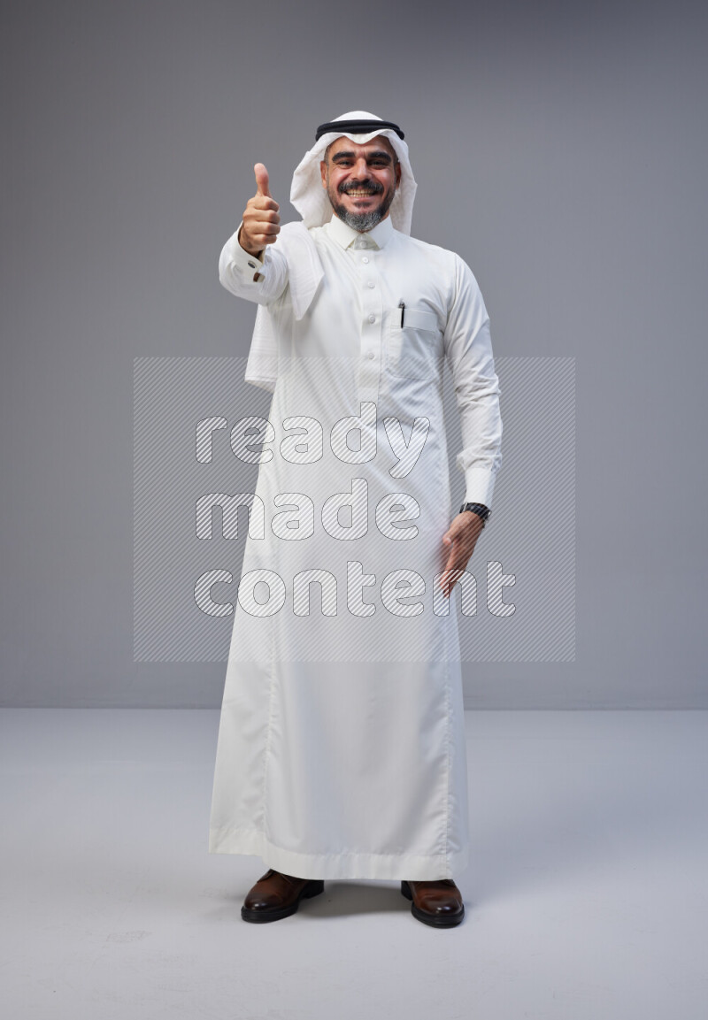 Saudi man Wearing Thob and white Shomag standing interacting with the camera on Gray background