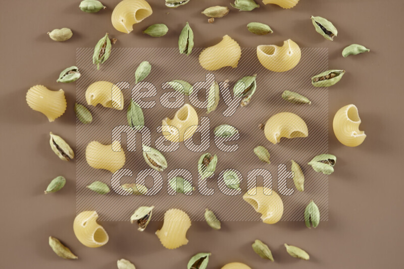 Raw pasta with different ingredients such as cherry tomatoes, garlic, onions, red chilis, black pepper, white pepper, bay laurel leaves, rosemary and cardamom on beige background