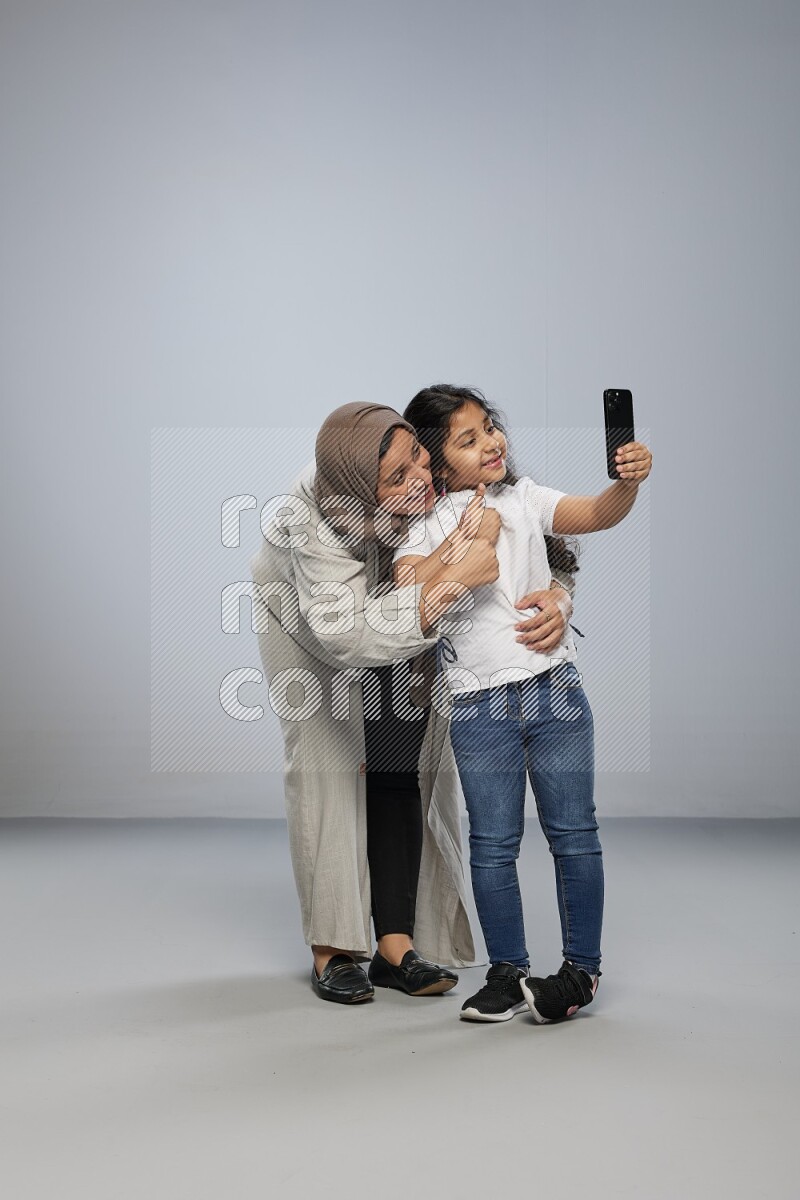 A girl standing taking selfie with her mother on gray background