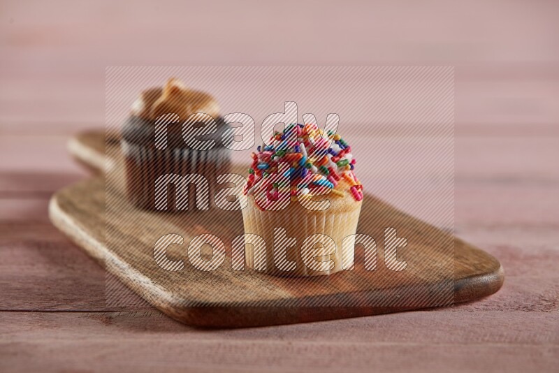 Vanilla mini cupcake topped with sprinkles on a wooden board