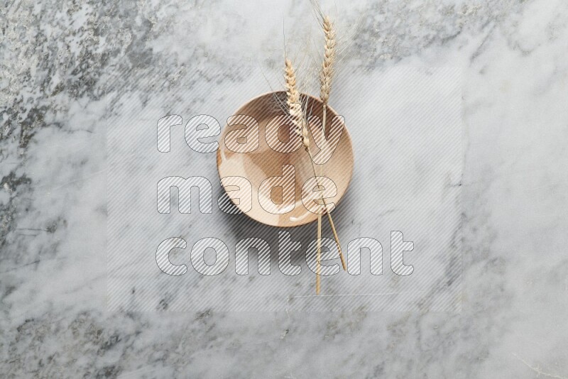 Wheat stalks on multicolored pottery plate on grey marble background