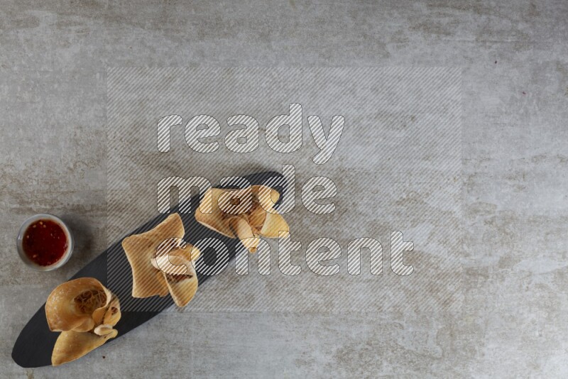 wonton cups with soy sauce ramkin on oval slate on grey textured counter top