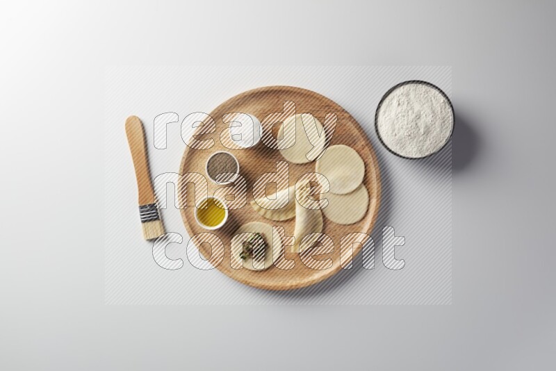 two closed sambosas and one open sambosa filled with meat while flour, salt, black pepper and oil with oil brush aside in a wooden dish on a white background