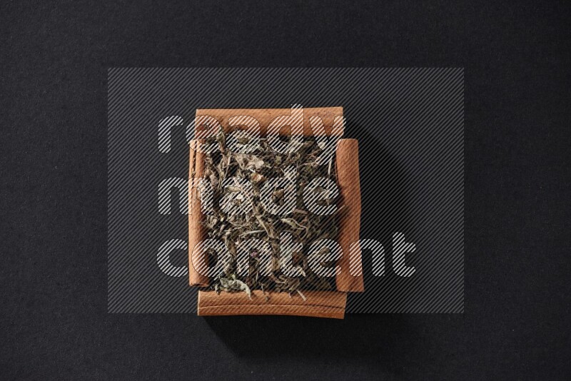 A single square of cinnamon sticks full of dried basil on black flooring