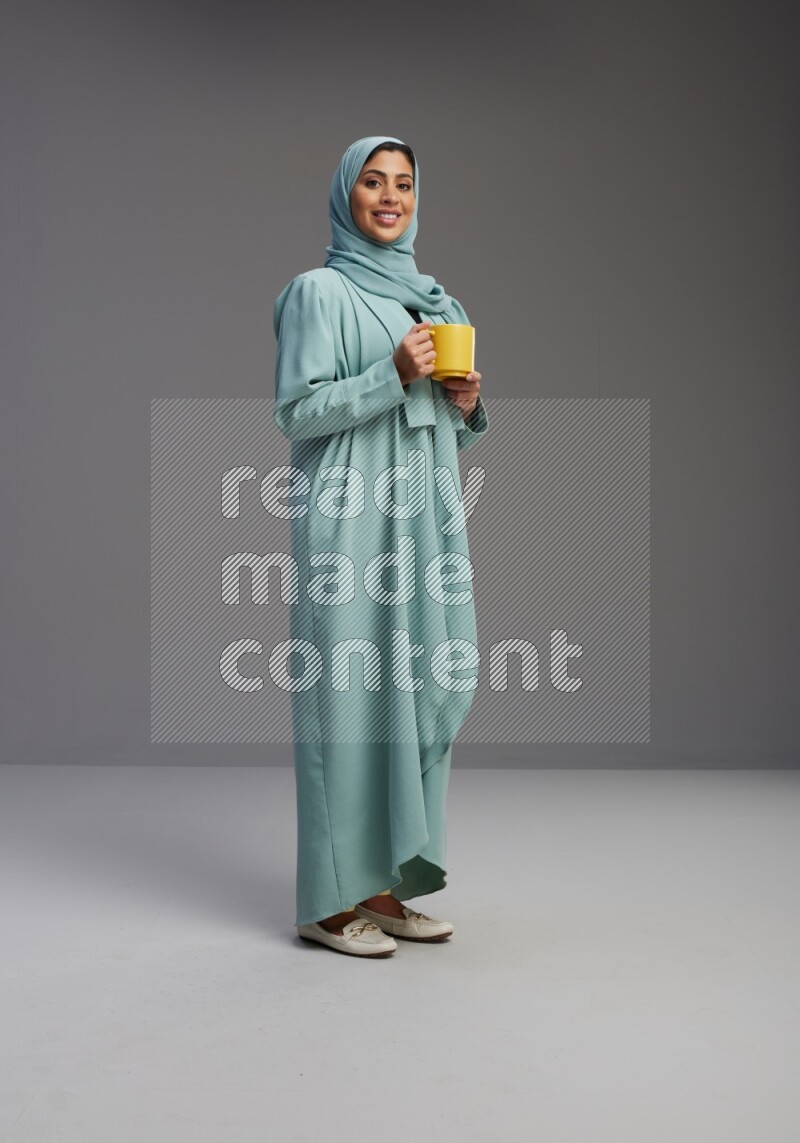 Saudi Woman wearing Abaya standing  holding a mug on Gray background