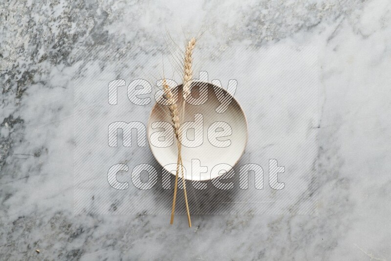 Wheat stalks on beige pottery plate on grey marble background