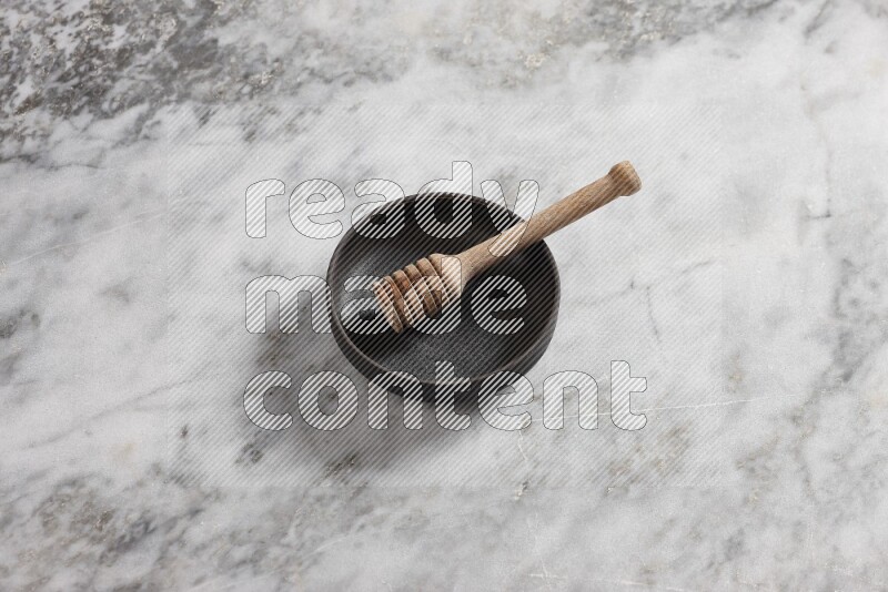Black pottery bowl with wooden honey dipper in it on grey marble background