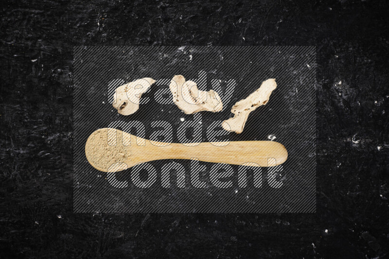 A wooden spoon full of ground ginger powder on black background