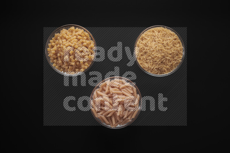 Different pasta types in glass bowls on black background