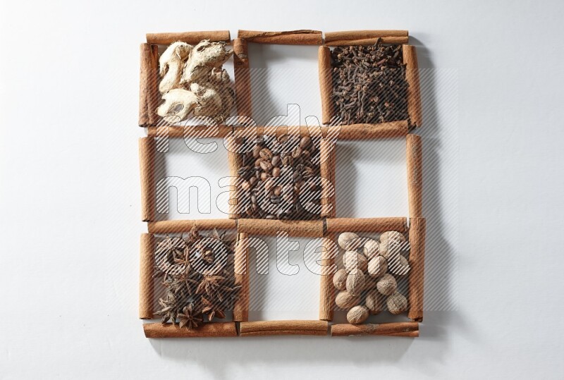 9 squares of cinnamon sticks full of coffee beans in the middle surrounded by dried mint, dried ginger, cardamom, star anise, cinnamon, nutmeg, dried basil and cloves on white flooring