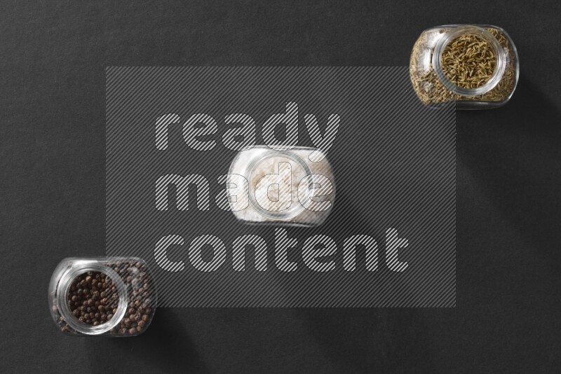 3 glass spice jars full of salt, black peppers and cumin on black flooring