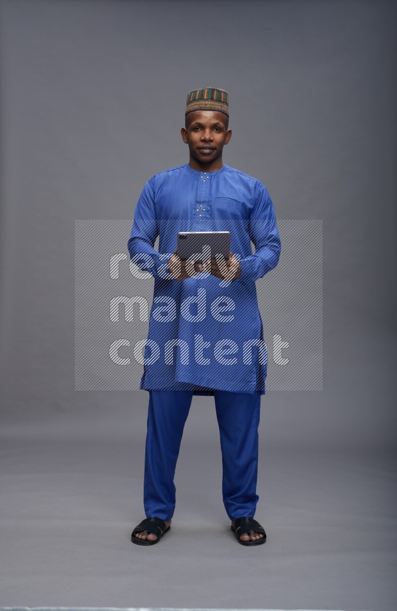 Man wearing Nigerian outfit standing working on tablet on gray background
