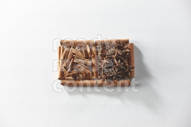 مربعان من أعواد القرفة ممتلئان باليانسون النجمي وقطع من القرفة علي خلفية بيضاء