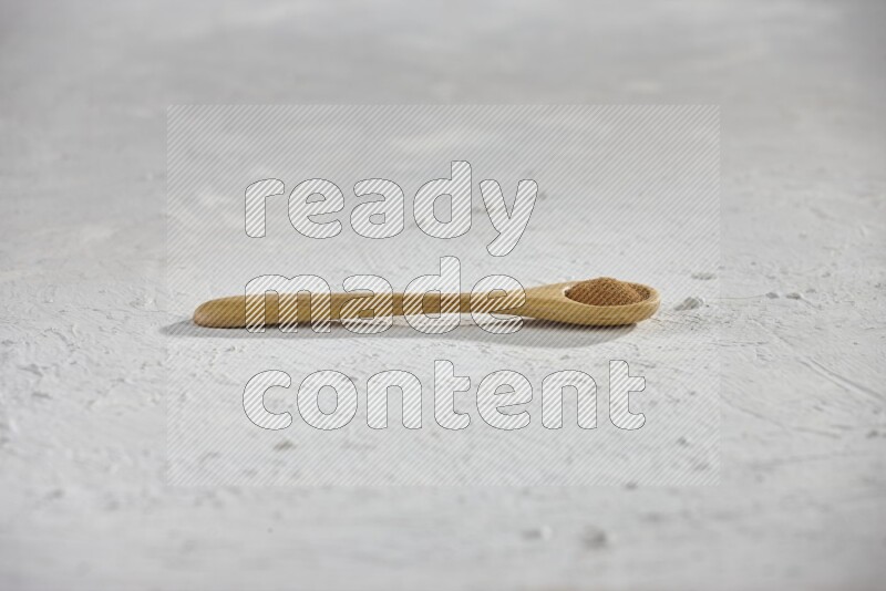 Cinnamon powder in a wooden spoon on a white background