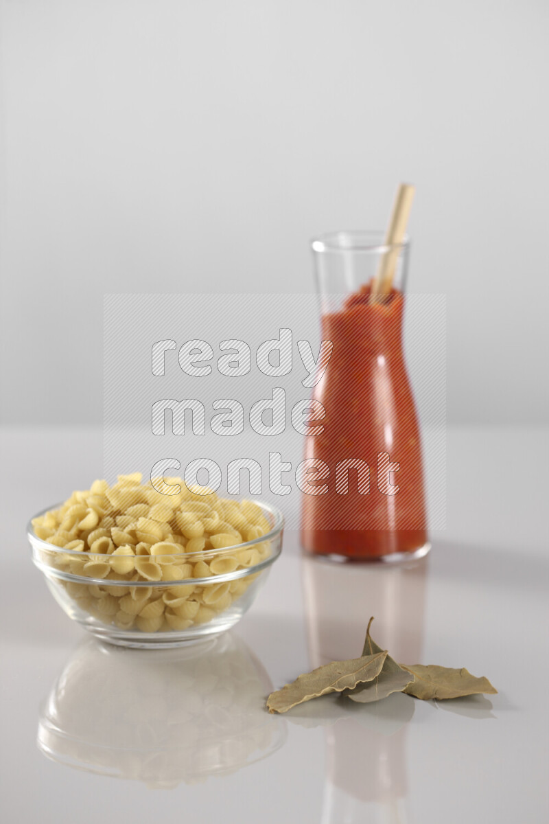 Raw pasta with tomatoe pasta with different ingredients such as cherry tomatoes, basil, garlic, bay laurel, cardamom, white pepper, black pepper, red chilis and wheat stalks on light grey background
