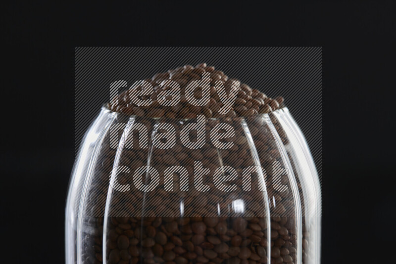 Brown lentils in a glass jar on black background