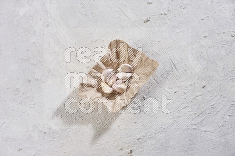 A crumpled piece of paper full of garlic cloves placed on a textured white flooring