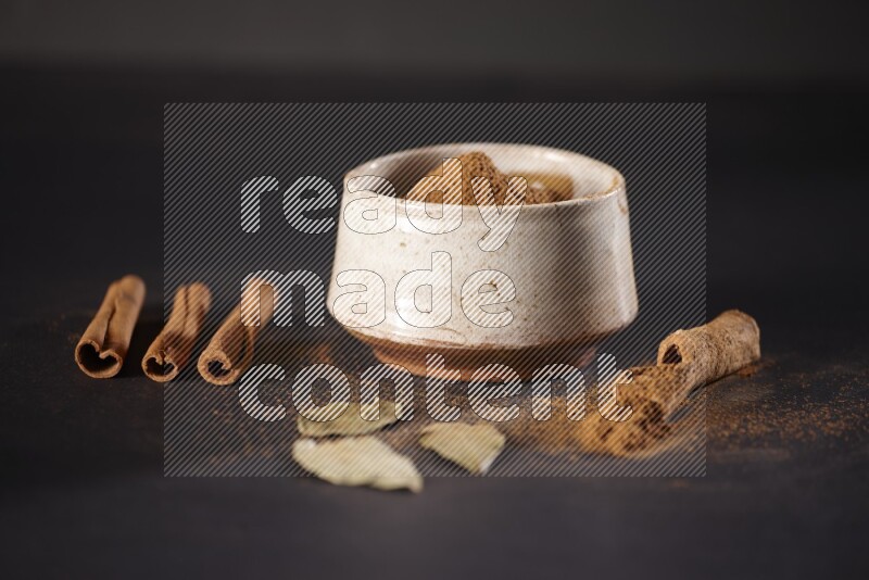 Cinnamon powder in a white pottery bowl and cinnamon sticks and laurel leaves on black background
