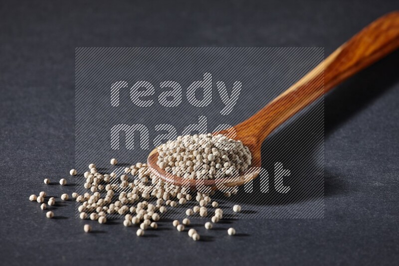 A wooden ladle full of white pepper beads on black flooring