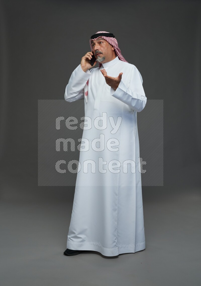 Saudi man with shomag Standing talking on phone on gray background