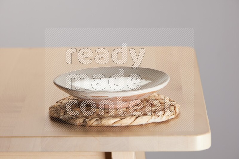 multi-colored pottery Plate placed on a small light colored straw placemat on the edge of wooden table