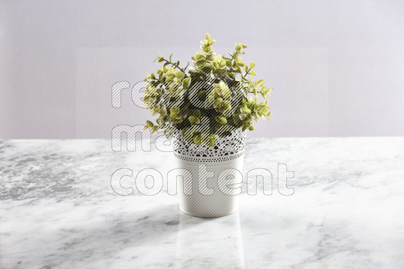 Green artificial plant in white decorative pot on grey marble background