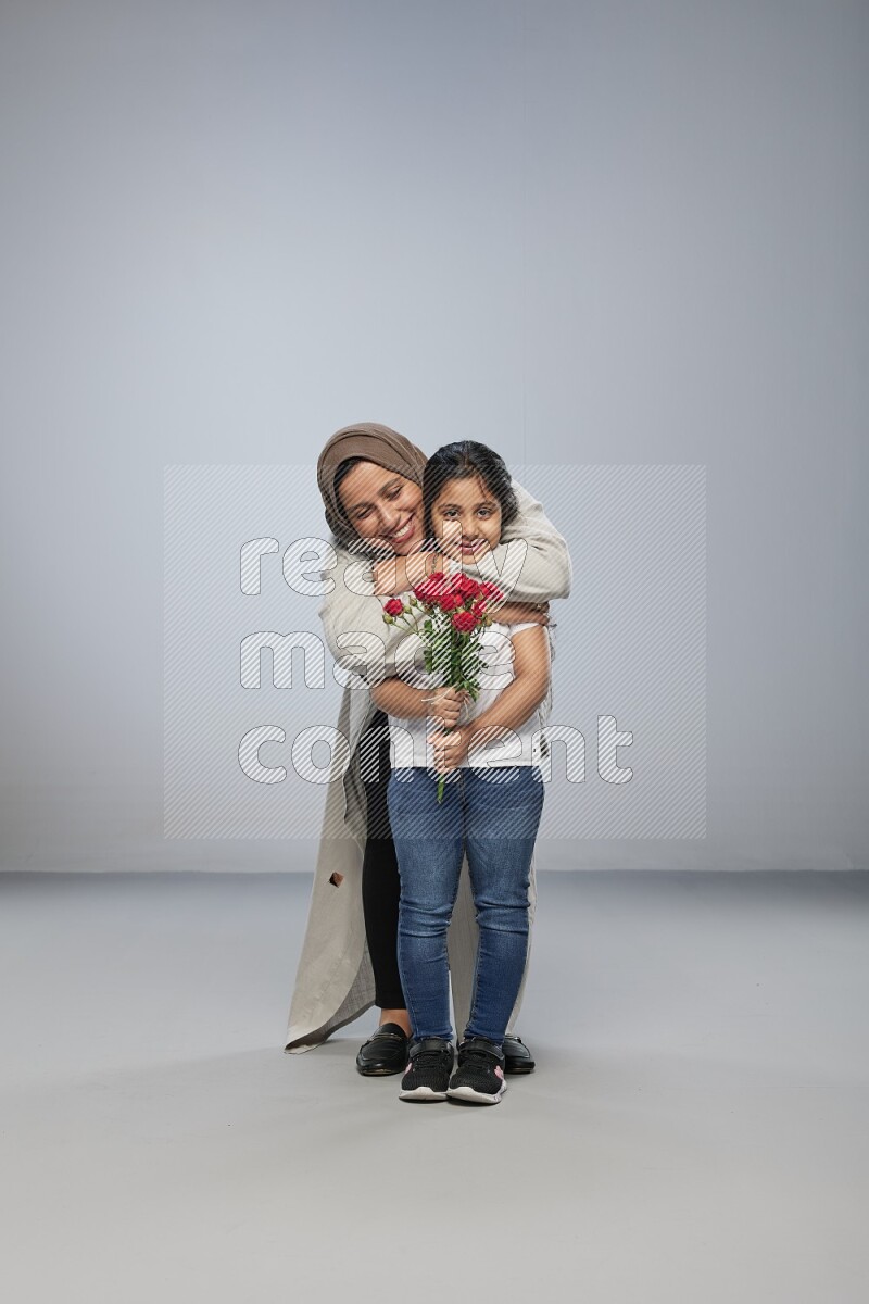 A girl standing giving flowers to her mother on gray background