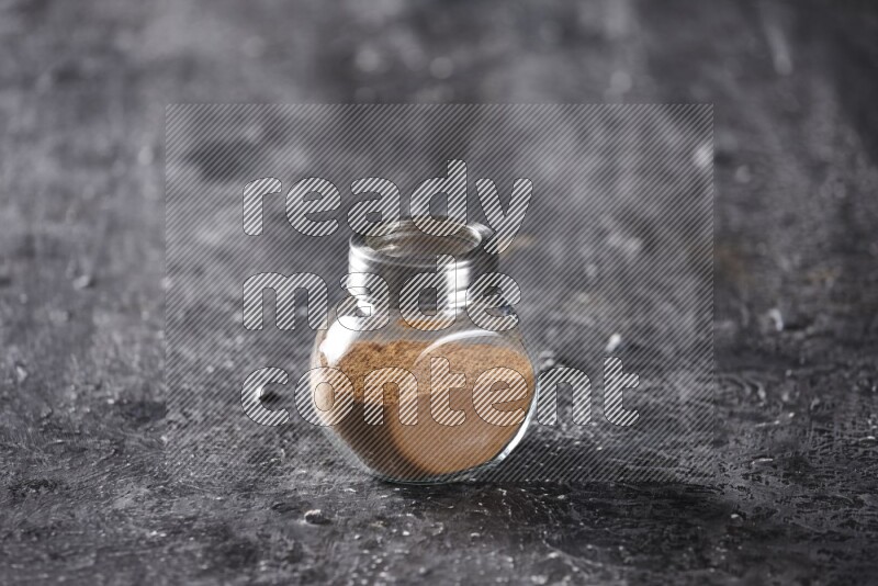 Herbal glass jar full of cinnamon powder on a textured black background