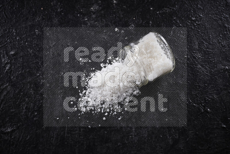 A glass jar full of coarse sea salt crystals on black background