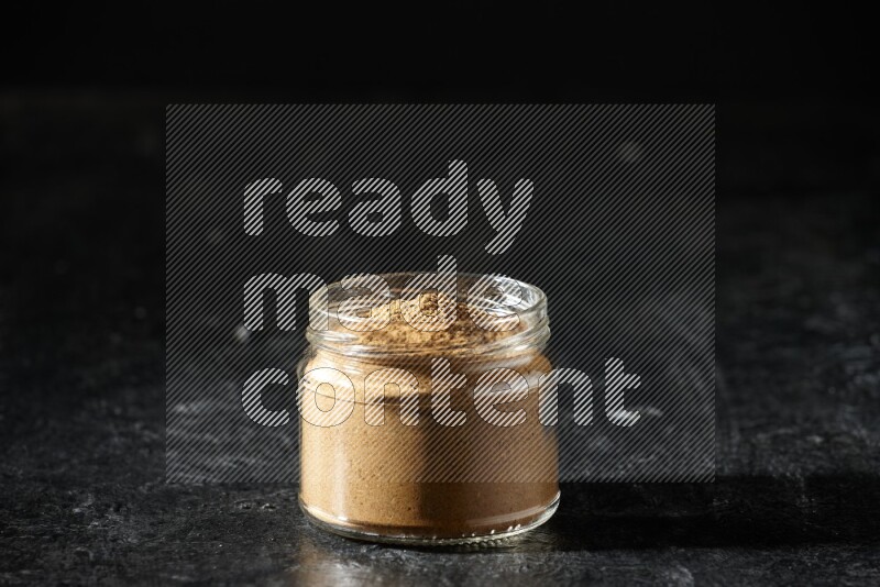 A glass jar full of allspice powder on a textured black flooring