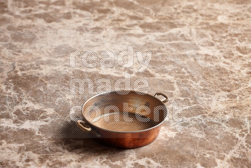 A small copper pan on beige marble background