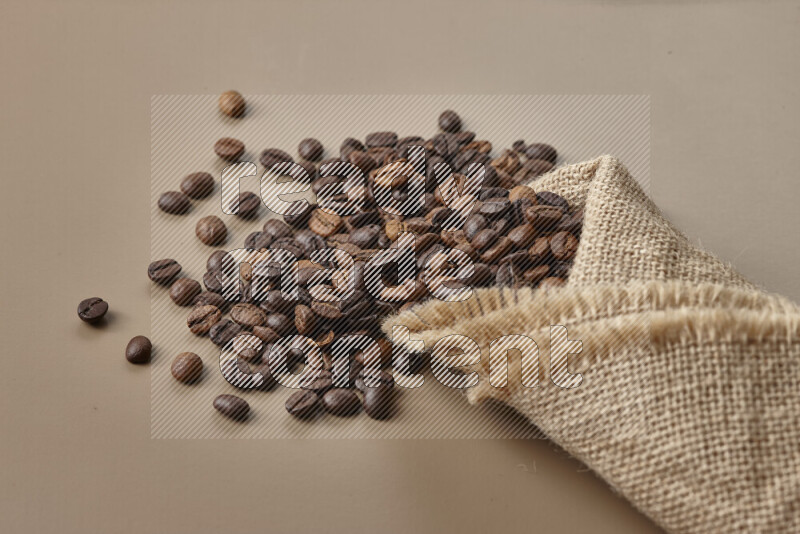 Spilled roasted coffee beans from its pack on beige background