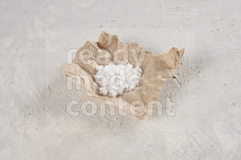 A crumpled piece of paper full of white salt on white background